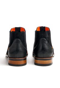 Bottes ankle en cuir noir et suède avec doublure orange, dotées d'un talon empilé marron et de panneaux latéraux élastiques pour un enfilage facile.