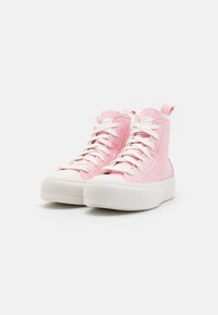 Wysokie sneakersy z jasnoróżowej kanwy, białą gumową podeszwą i białymi sznurówkami, z pętelką z tyłu ułatwiającą zakładanie.
