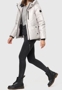 Vadderad silverjacka med huva, framdragkedja och svarta accenter. Svarta skinny jeans och svarta snörboots med kraftiga sulor.