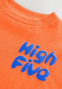 Pomarańczowa bawełniana koszulka z teksturowanym niebieskim nadrukiem "High Five". Żebrowany kołnierz i gładka faktura materiału.