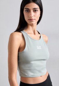 Lysegrønn crop top i elastisk stoff, med rund hals og brede ermer. Liten hvit logo på brystet. Enkel design, ingen mønstre.