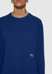 Niebieska sportowa bluzka z długim rękawem, wykonana z fakturowanej tkaniny, z okrągłym dekoltem. Posiada białe logo na dolnej części przodu. Stylowy, aktywny krój.