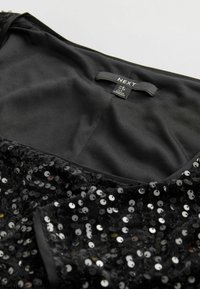Robe noire à paillettes avec un col en satin. Présente des paillettes rondes dans des teintes variées réfléchissant la lumière. Étiquette de marque visible.