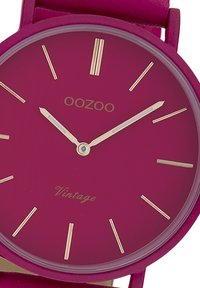Montre avec bracelet en silicone violet et cadran rond violet. Index et aiguilles dorés, affichant un design minimaliste avec le texte "OOZOO Vintage".