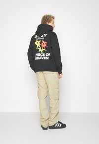 Felpa nera con un grande e colorato motivo floreale e testo sul retro, abbinata a pantaloni cargo beige e sneakers neri.