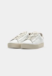 Sneakers bianchi in pelle con suola in gomma beige, lacci piatti e finitura liscia. Presentano un piccolo accento sul tallone e una marca laterale.