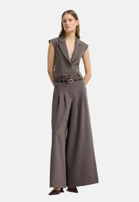 Grijze twee-delige outfit bestaande uit een mouwloze, cropped blazer met een enkele knoop en wijde, geplooide broek, aangevuld met een bijpassende riem.