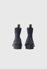 Bottines en daim bleu marine avec une finition lisse, des panneaux élastiques sur les côtés et des semelles en caoutchouc noir. Comprend une languette avec le logo de la marque au talon.