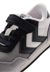 Sneaker aus Mesh, Wildleder und synthetischen Materialien. Mit schwarzen, weißen und grauen Farben, Schnürsenkeln und einem Klettverschluss. Chevron-Akzente.