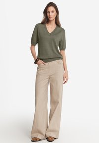 Kortärmad, olivgrön V-ringad tröja med en åtsittande nederkant, parat med beige vida byxor med vertikala ränder och bruna sandaler.