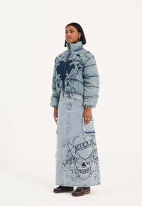 Polstret denimjakke i lyseblå med høj krave og en mørkeblå grafik; lang denimskirt med broderede kranier, hjerter og tekstdetaljer.