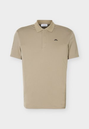 Beiges Poloshirt mit kurzen Ärmeln, Kragen und kleinem schwarzem Logo auf der linken Brust, präsentiert vor weißem Hintergrund.