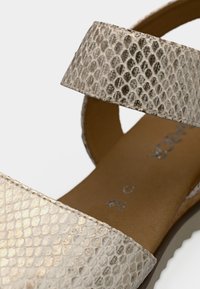 Πλατφόρμα σανδάλι με υφή, επάνω μέρος από ψεύτικο δέρμα φιδιού σε ανοιχτό μπεζ χρώμα και φαρδιά λουριά. Μαλακό καφέ πέλμα με διακριτική λεπτομέρεια λογοτύπου.