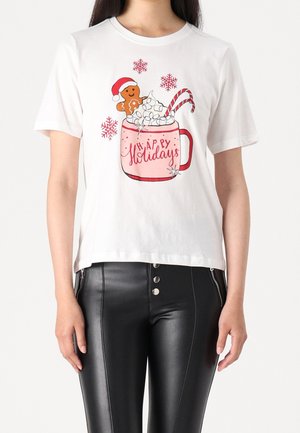 Kobieta w białej koszulce z różowym kubkiem, piankami marshmallow, laski cukrowej, pierniczkiem w czapce Świętego Mikołaja, czerwonymi płatkami śniegu i napisem „Wesołych Świąt”.