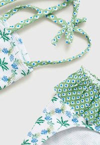 Bikini top s cvjetnim uzorkom u zelenoj i plavoj boji, od strukturiranog bijelog materijala, s podesivim vezicama i naboranim detaljima na rubovima.