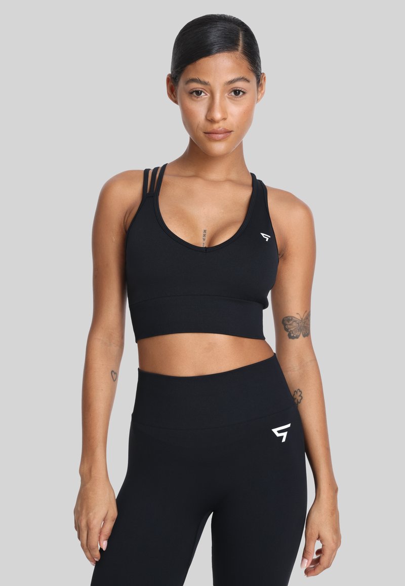 Zwarte sportbeha met een V-hals, drie dunne banden over de schouders en een cropped ontwerp. Glad textuur en logo in het wit aan de linkerkant.