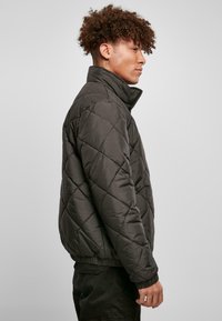 Quilted sort pufferjakke med høj krave, elastiske manchetter og kant, der har en glat overflade og diamantmønster over det hele.