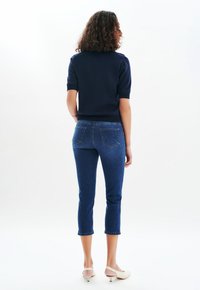 Granatowy sweter z krótkim rękawem w zestawie z wąskimi, ciemnoniebieskimi jeansami do kostek, które mają dwie tylne kieszenie i podwinięte mankiety.