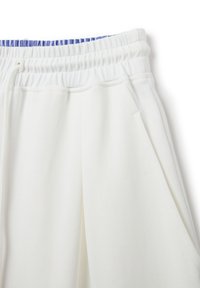 Pantalones de chándal blancos con piernas anchas, que cuentan con una cintura elástica con acentos azules y bolsillos laterales. Se puede apreciar una textura de tela suave.