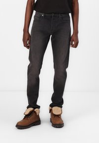 Jeans negros ajustados con una textura ligeramente desgastada, combinados con botas marrones con cordones que cuentan con un forro de pelo sintético y suelas resistentes.