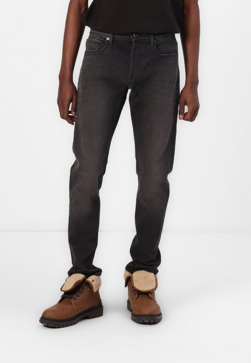 Jeans negros ajustados con una textura ligeramente desgastada, combinados con botas marrones con cordones que cuentan con un forro de pelo sintético y suelas resistentes.
