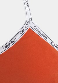 Top cropped laranja da Calvin Klein em tecido elástico texturizado, com alças brancas com a marca e um design elegante e ajustado.