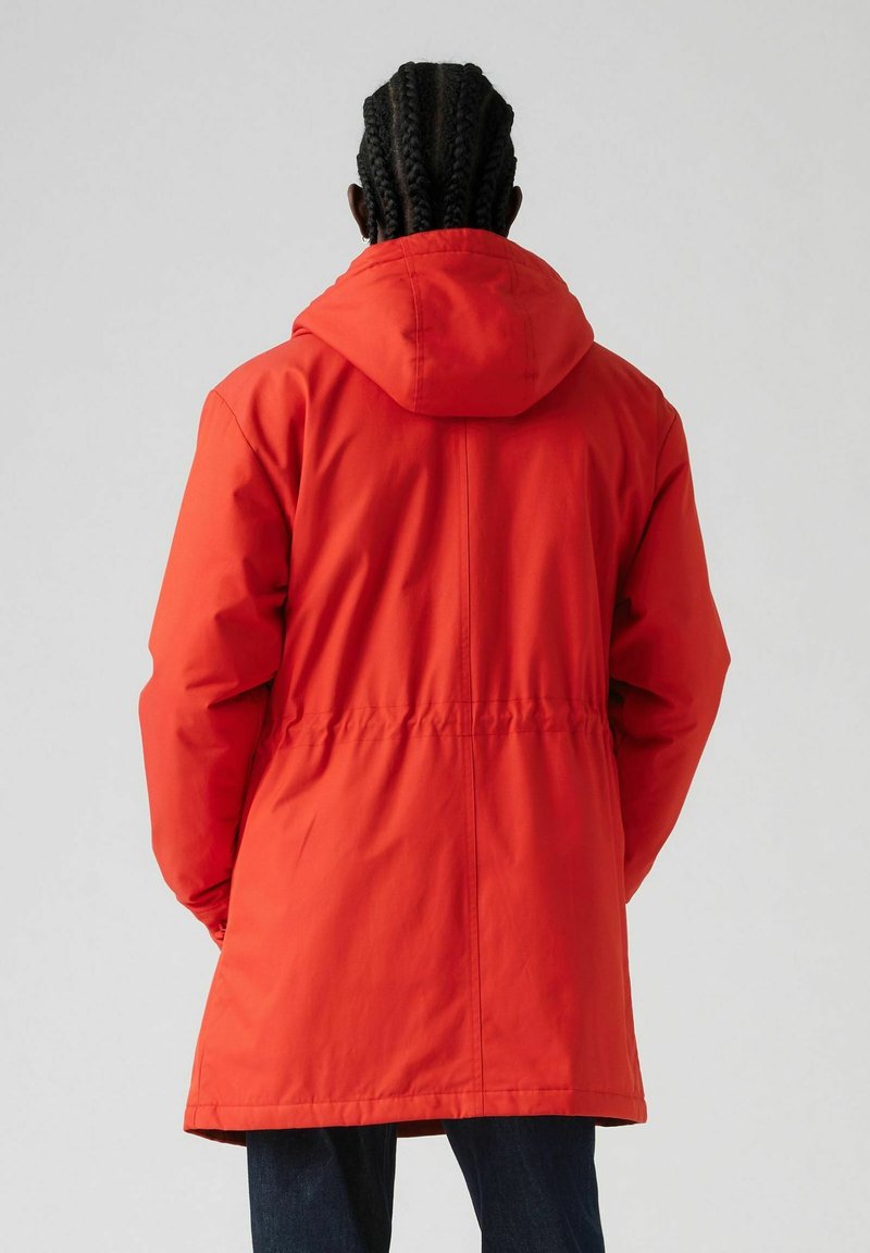 Rode gewatteerde parka met een taillering, een gladde, waterafstotende stof en een middellange snit. Beschikt over een afneembare capuchon en een ritssluiting.
