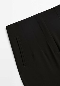 Gros plan d'un pantalon noir montrant une poche passepoilée latérale et des détails de couture verticale sur un tissu à texture lisse.