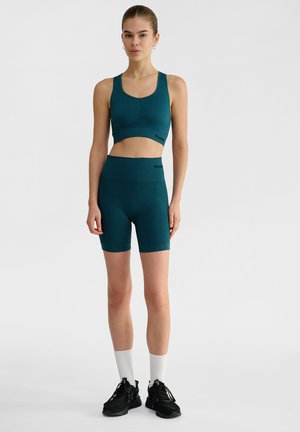 Türkise Sport-BH und passende hochgeschnittene Shorts aus dehnbarem Stoff. Besitzt eine gerippte Textur und Logodetails am Bund.