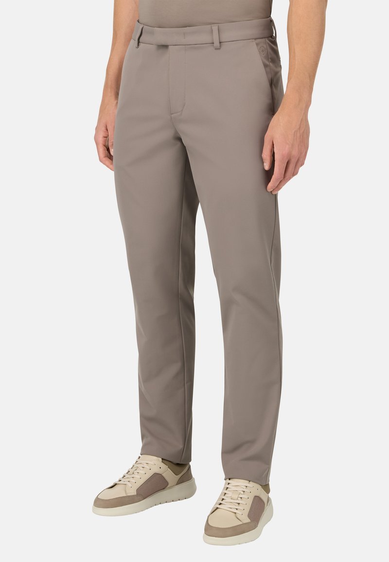 Pantaloni color marrone chiaro con un design snello, realizzati in tessuto liscio, con passanti per cintura e tasche laterali, abbinati a sneakers beige.