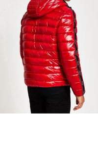 Doudoune rouge avec une finition brillante, motif matelassé et capuche. Dotée de bandes noires sur les côtés avec des accents textuels et une coupe ajustée.