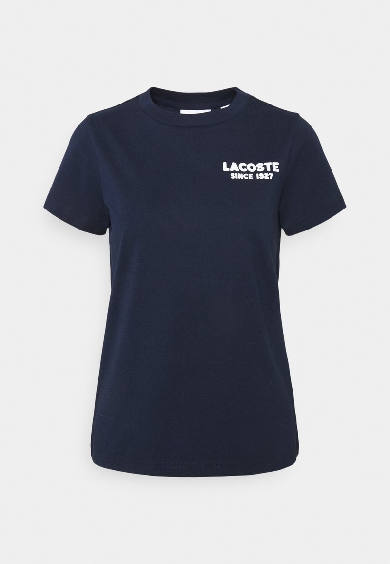 T-shirt en coton bleu marine à manches courtes et col rond, avec le texte blanc "LACOSTE SINCE 1927" sur la poitrine.