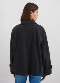 Schwarze, übergroße Jacke mit spitzem Kragen, abfallenden Schultern und knopfbaren Manschetten. Besitzt eine glatte Textur und minimalistisches Design.