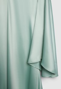 Light green satin fabric with flowing draped folds and smooth texture, hanging vertically against a plain light background.