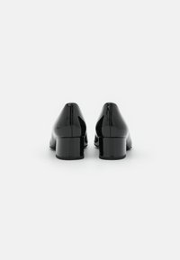 Scarpe con tacco a blocco in vernice nera, con un design a punta elegante, caratterizzate da una superficie liscia e riflettente e da dettagli di cucitura minimi.