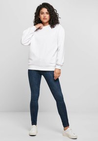 Valkoinen collegepaita, jossa on pitkät ilmatäytetyt hihat ja pyöreä pääntie, yhdistetty tummansinisiin kapealahkeisiin farkkuihin ja valkoisiin lenkkareihin. Sileä puuvillainen materiaali.