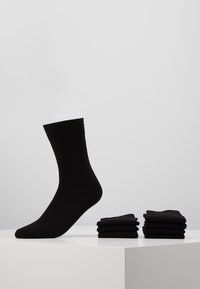 Chaussettes en coton noir avec un bord côtelé, présentées une à la verticale et huit soigneusement empilées sur une surface blanche, texture lisse et forme uniforme.