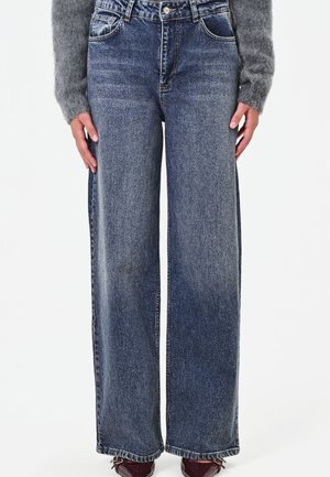 Jeans in denim blu a gamba dritta e vita alta, indossati con un maglione grigio peloso e scarpe marroni scure a punta.