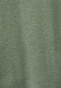 Gros plan sur un tissu doux vert chiné avec une texture fine de tricot visible et une couture apparente près du bord inférieur.