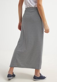 Jupe maxi rayée gris et blanc, en tissu doux, avec une taille ajustée et un design légèrement évasé, associée à des baskets bleu marine.