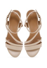 Beige high-heeled sandals with crisscross straps, smooth texture, and a shiny platform. Buckle accent on ankle strap.