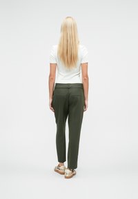 Zielone spodnie na miarę o prostych nogawkach, teksturowanej tkaninie i tylnych kieszeniach, zestawione z casualowym obuwiem i dopasowanym białym topem.