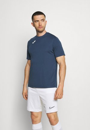 Mørkeblå atletisk t-shirt lavet af letvægtsstof, der har et hvidt logo på brystet, parret med hvide shorts og sokker.