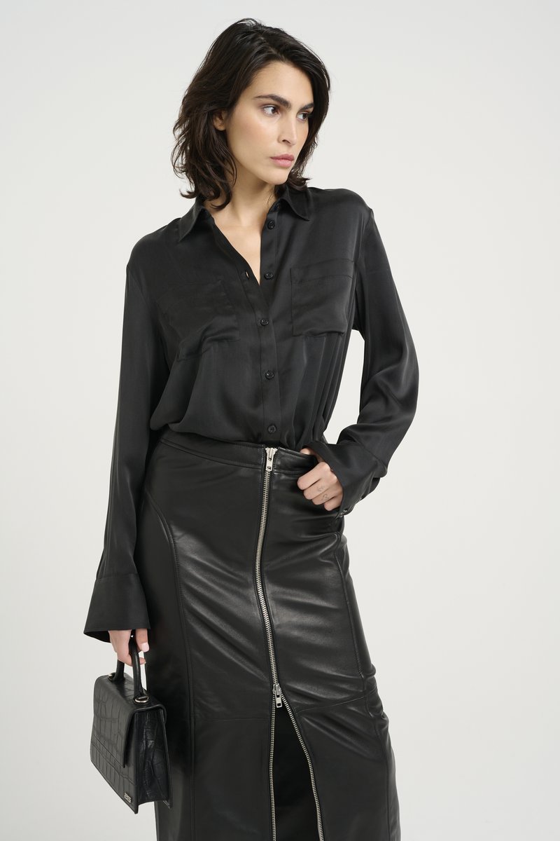 Black satin button-down shirt with two chest pockets, paired with a black leather zippered skirt and textured black handbag.