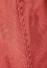 Close-up van rode stof met zichtbare naadstiksels die verticaal nabij het midden lopen.