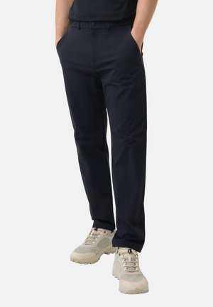 Marineblaue Hose aus leichtem Stoff mit geradem Schnitt, ausgestattet mit Seitentaschen und einem Knopfverschluss an der Taille. Kombiniert mit beigefarbenen Sneakers.