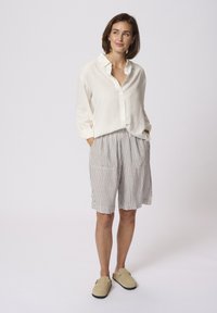 White linen button-up shirt with a collar, paired with gray striped shorts. Beige slip-on shoes. Simple design, casual fit.
