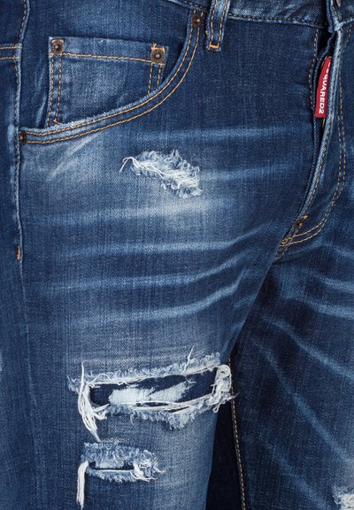 Versleten blauwe spijkerbroek met gescheurde plekken op de dijen, voorzien van contrasterende stiksels en een klein label op de zak.