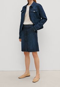 Chaqueta de denim azul oscuro con dos bolsillos en el pecho, combinada con una falda de denim a juego. Corte ajustado, longitud hasta la rodilla, textura suave y detalles mínimos.