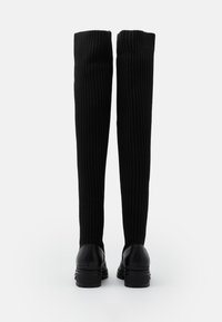 Musta polven ylle ulottuva saappaat ribbitetystä kankaasta, muotoiltu design. Ominaisuuksia pyöreä kärki ja tukevat mustat kumipohjat vakauden takaamiseksi.